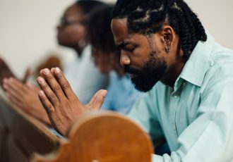 Black man praying with family in church pew