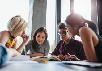 Group of young people sitting at table reading books
