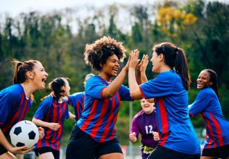 Happy women's soccer team celebrating victory after playing a match at the stadium.