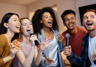 Sing it. Enthusiastic group of friends singing with microphone while playing karaoke at home